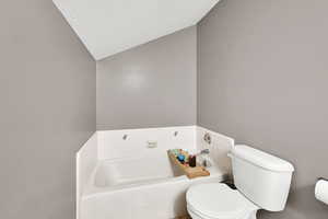 Bathroom featuring a bath, vaulted ceiling, and toilet