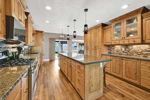 Kitchen featuring baseboards, a center island, tasteful backsplash, light wood finished floors, and appliances with stainless steel finishes