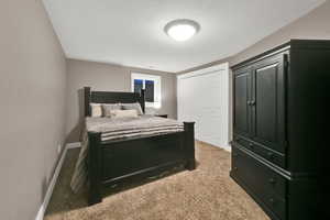 Bedroom with a textured ceiling, baseboards, light carpet, and a closet