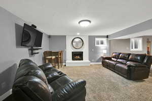 Living room featuring carpet flooring, a textured ceiling, baseboards, and a fireplace