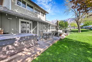 Wooden terrace with outdoor dining space, a hot tub, grilling area, a mountain view, and a lawn