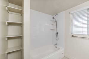 Bathroom featuring a textured ceiling, baseboards, and washtub / shower combination