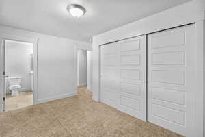 Unfurnished bedroom with a closet, baseboards, ensuite bathroom, and light carpet