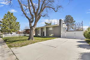View of front facade featuring a front yard, a chimney, fence, brick siding, and a gate