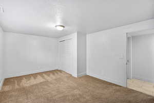 Unfurnished bedroom featuring light colored carpet, a textured ceiling, baseboards, and a closet