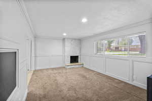 Unfurnished living room featuring a textured ceiling, a fireplace, ornamental molding, carpet, and a decorative wall