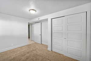 Unfurnished bedroom featuring baseboards, a textured ceiling, and light carpet