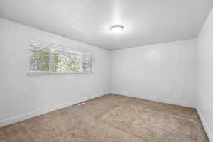 Unfurnished room featuring baseboards, light colored carpet, a textured ceiling, and visible vents