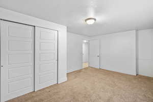 Unfurnished bedroom featuring a textured ceiling, baseboards, carpet, and a closet