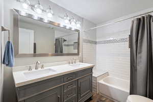 Bathroom with double vanity, a sink, shower / tub combo, and wood finished floors