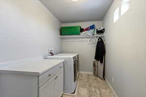 Clothes washing area with baseboards, cabinet space, and washer and dryer
