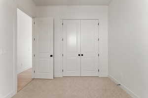 Unfurnished bedroom featuring baseboards, light carpet, and a closet