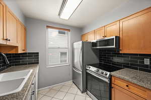 Kitchen with dark countertops, baseboards, a sink, appliances with stainless steel finishes, and backsplash