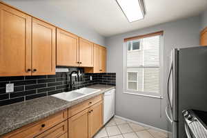 Kitchen featuring freestanding refrigerator, decorative backsplash, stove, a sink, and dishwasher