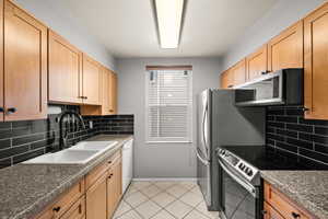 Kitchen with decorative backsplash, baseboards, a sink, light tile patterned floors, and stainless steel appliances