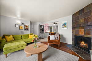 Living area featuring baseboards, ceiling fan, a tiled fireplace, and wood finished floors