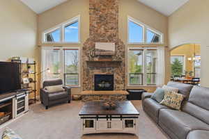 Carpeted living room featuring plenty of natural light, a towering ceiling, a chandelier, and a stone fireplace