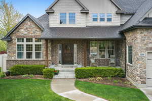 View of front of house featuring board and batten siding, roof with shingles, stone siding, and a front yard