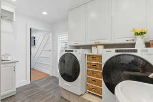 Washroom with cabinet space, recessed lighting, washer and clothes dryer, and wood finished floors