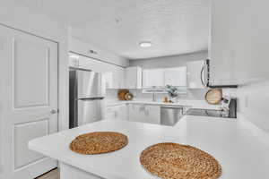 Kitchen with appliances with stainless steel finishes, light countertops, a textured ceiling, white cabinetry, and a peninsula