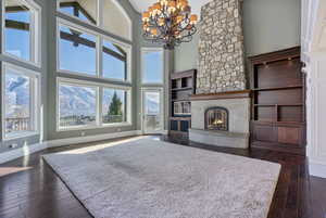 Living room featuring dark wood-style flooring, a towering ceiling, a fireplace, baseboards, and a notable chandelier