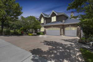View of front of house featuring a shingled roof, an attached garage, stone siding, a chimney, and concrete driveway