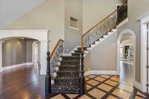 Stairway with baseboards, arched walkways, a high ceiling, and hardwood / wood-style flooring