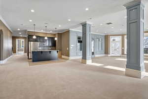 Unfurnished living room with crown molding, light carpet, recessed lighting, baseboards, and decorative columns