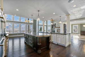Kitchen with decorative columns, baseboards, recessed lighting, a large island with sink, and dark wood finished floors