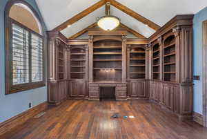 Interior space with built in desk, baseboards, lofted ceiling, visible vents, and dark wood-style floors