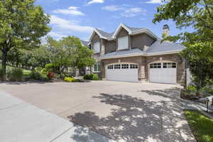 View of front facade featuring stone siding, stucco siding, a chimney, a shingled roof, and driveway