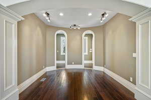 Unfurnished room featuring arched walkways, rail lighting, baseboards, dark wood-type flooring, and visible vents