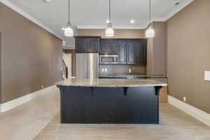 Kitchen with a breakfast bar, baseboards, a center island, light stone counters, and appliances with stainless steel finishes