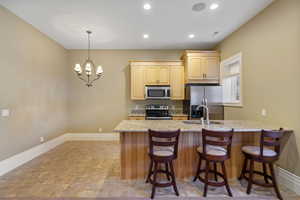 Kitchen featuring light brown cabinetry, a breakfast bar, baseboards, a sink, and stainless steel appliances