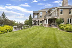 Rear view of house featuring a balcony, stone siding, a patio, stucco siding, and a lawn