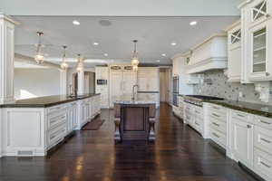 Kitchen featuring a breakfast bar area, custom range hood, a large island with sink, a sink, and appliances with stainless steel finishes