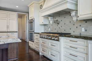 Kitchen featuring custom exhaust hood, dark wood-style floors, dark stone countertops, backsplash, and stainless steel appliances