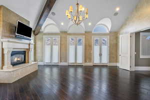 Unfurnished living room featuring an inviting chandelier, hardwood / wood-style flooring, french doors, lofted ceiling with beams, and a premium fireplace