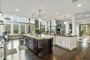 Kitchen with a notable chandelier, ornamental molding, a large island, decorative columns, and dark wood-style floors