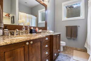 Bathroom featuring double vanity, toilet, baseboards, and a sink