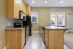 Kitchen featuring light brown cabinetry, baseboards, light stone counters, a sink, and appliances with stainless steel finishes