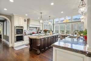 Kitchen with a kitchen island with sink, appliances with stainless steel finishes, a sink, custom range hood, and recessed lighting