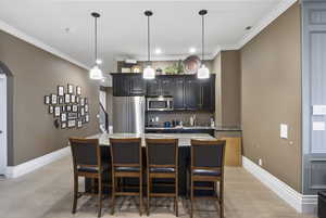 Kitchen featuring arched walkways, appliances with stainless steel finishes, a breakfast bar, and ornamental molding