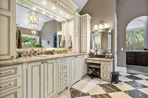 Full bath with double vanity, a sink, a chandelier, and vaulted ceiling