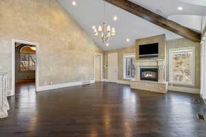 Unfurnished living room with high vaulted ceiling, a chandelier, dark wood finished floors, baseboards, and a high end fireplace