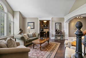 Living room with dark wood-style flooring, arched walkways, vaulted ceiling, and decorative columns