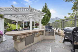 View of patio featuring fence, a pergola, area for grilling, exterior kitchen, and a mountain view