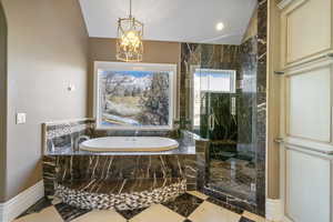 Bathroom featuring a notable chandelier, marble finish floor, baseboards, a garden tub, and a stall shower