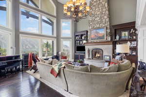Living area featuring a healthy amount of sunlight, a towering ceiling, a large fireplace, wood-type flooring, and an inviting chandelier
