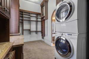 Washroom featuring light colored carpet, baseboards, cabinet space, and stacked washer / drying machine